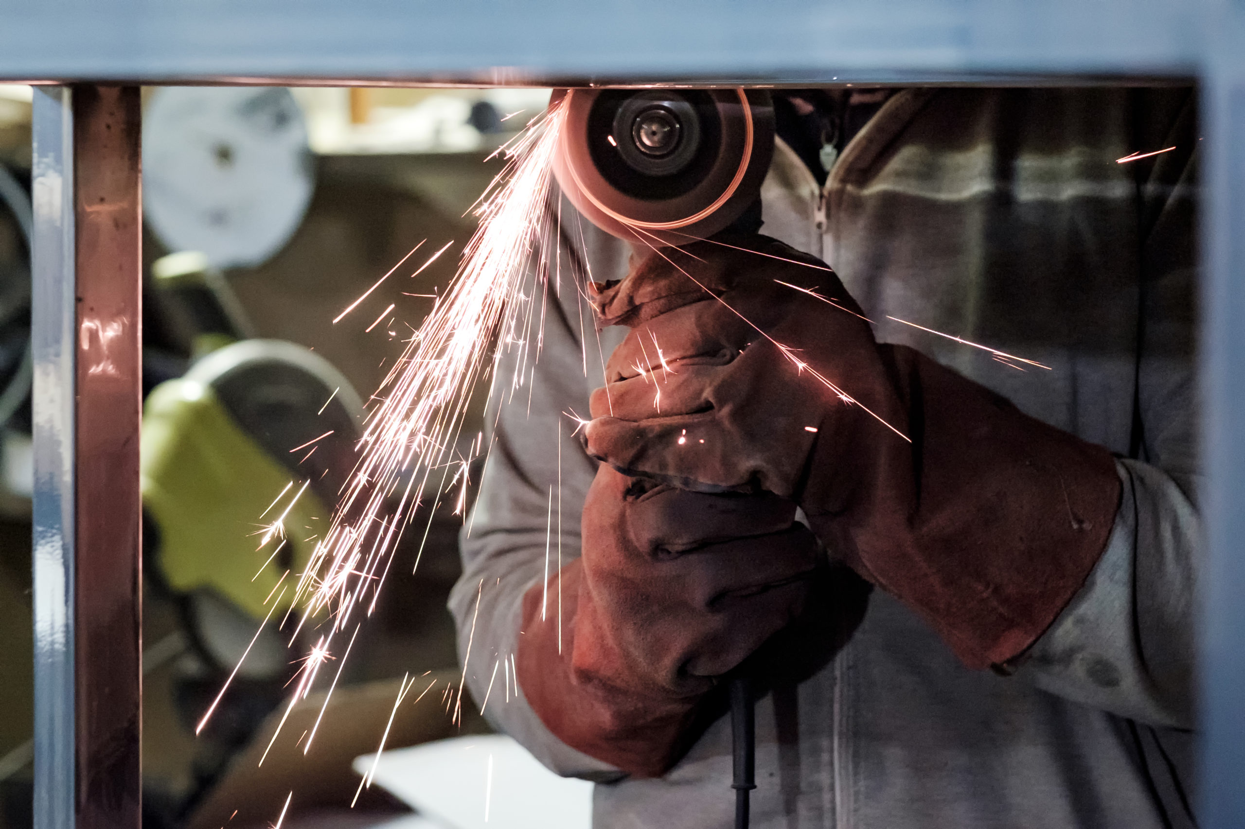Man in protective gloves cutting metal using angle grinder making sparks in workspace